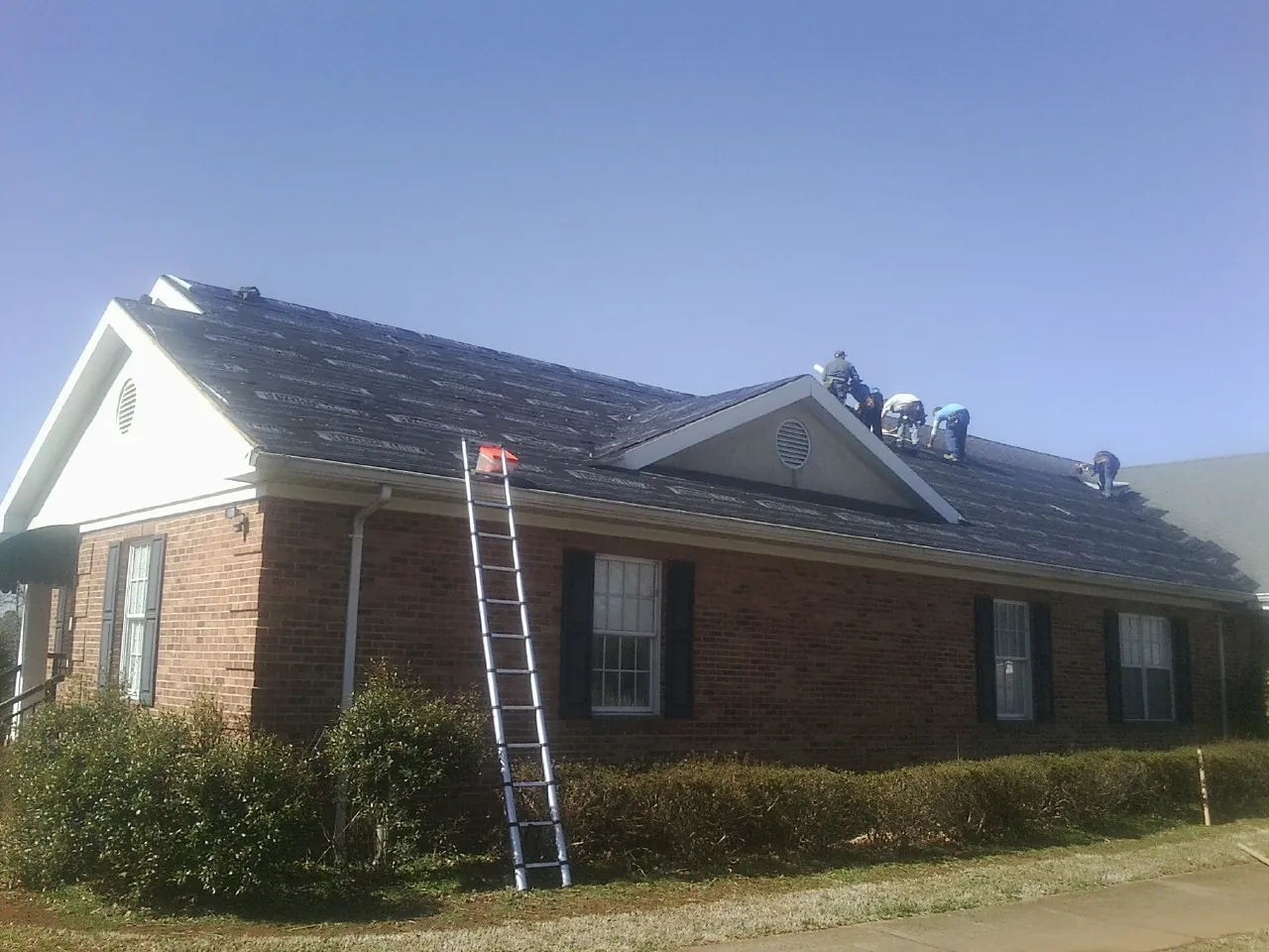 Crew tearing shingles off a brick ranch roof with a ladder set — Emergency Roof Repair work by our crew in Red Feather Lakes