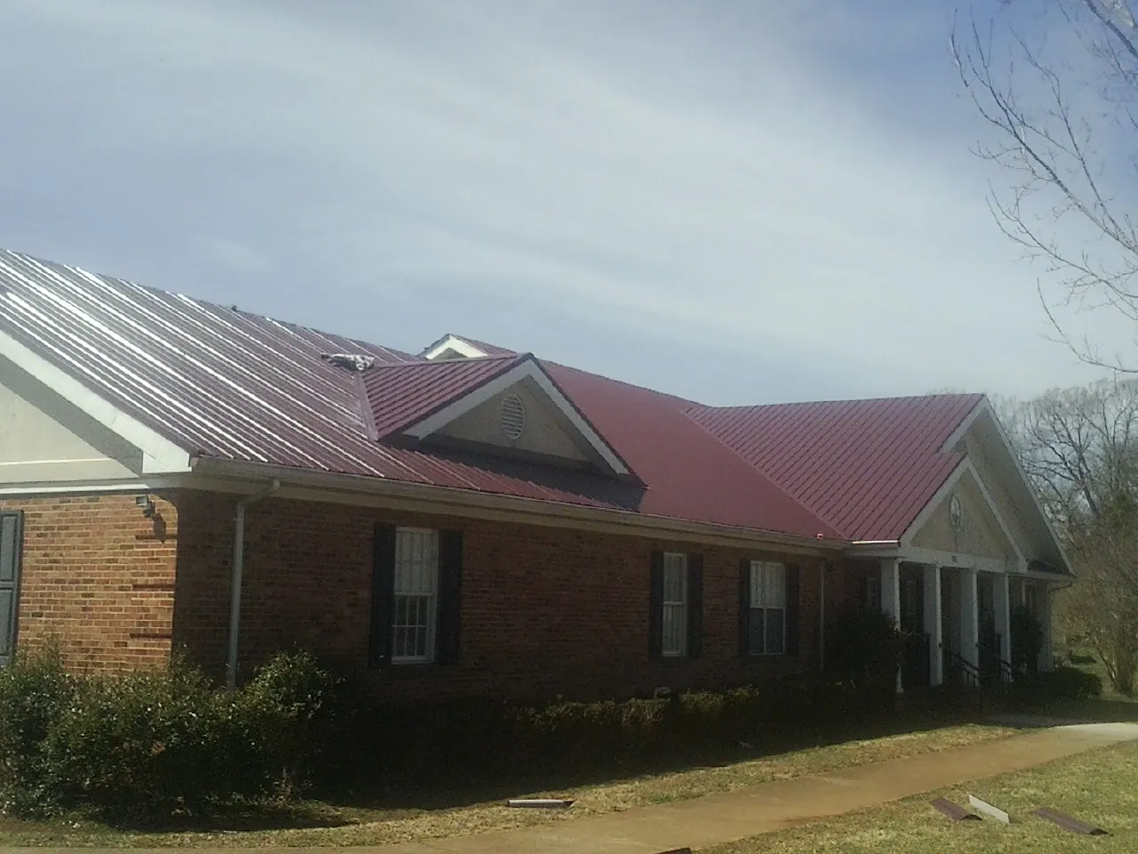 Red metal roof with gabled entries on a long brick building, from a Hail Damage Roof Repair job in Red Feather Lakes