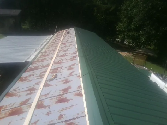 Old rusted panels beside newly installed green metal roofing — Wind Damage Roof Repair by Roofing Brothers in Red Feather Lakes