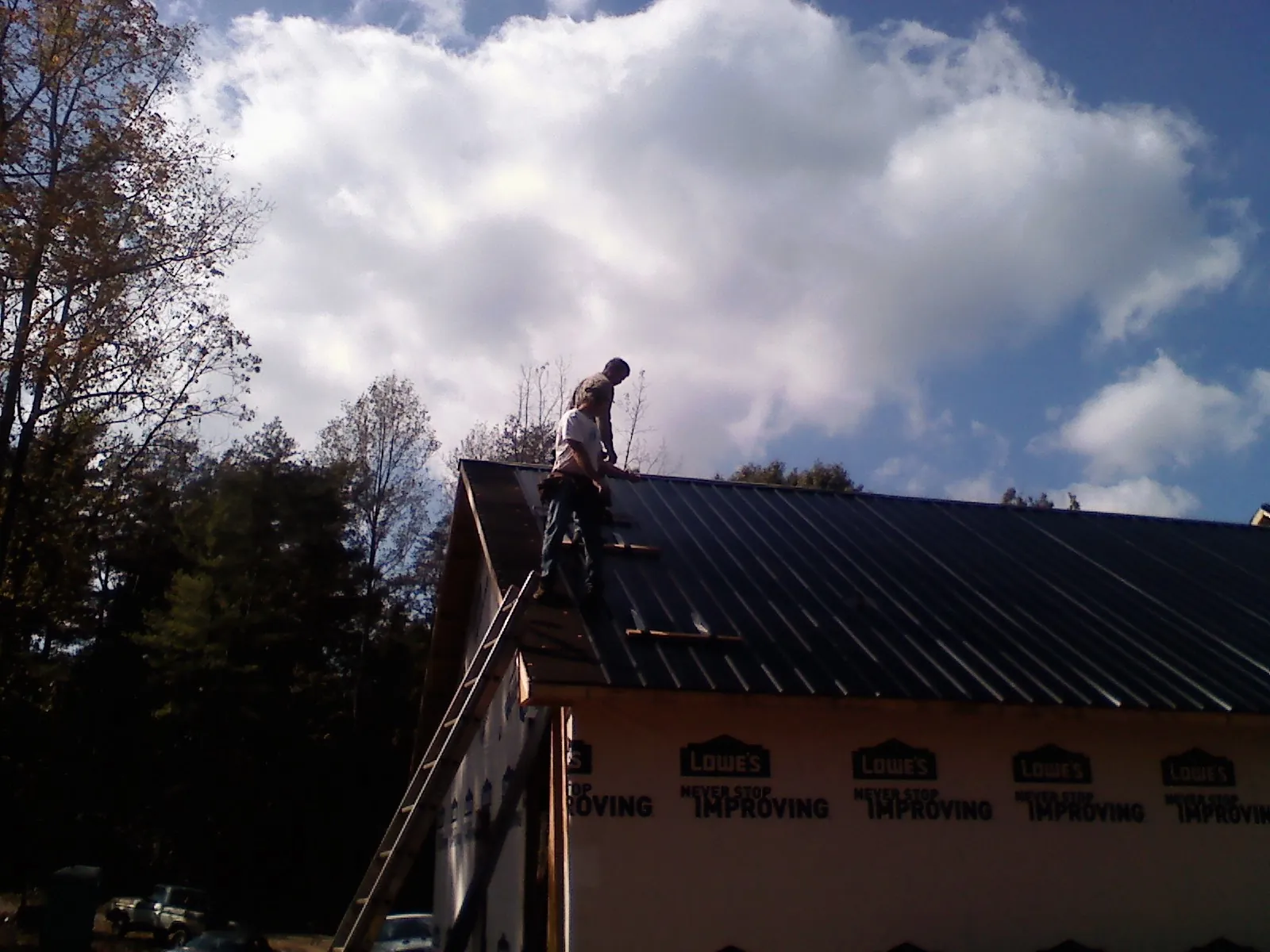Roofer fastening dark metal panels high against a cloudy sky, from a Roof Inspection job in Red Feather Lakes