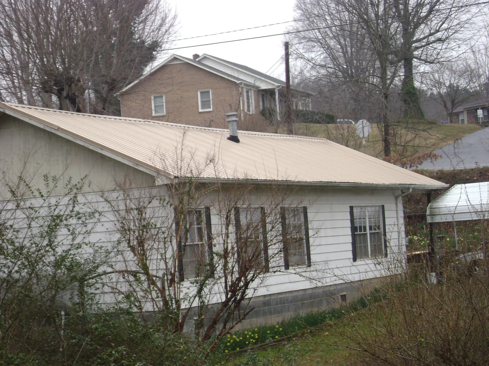 Tan metal roof on a white sided house set into a hillside — Commercial Roofing by Roofing Brothers in Red Feather Lakes